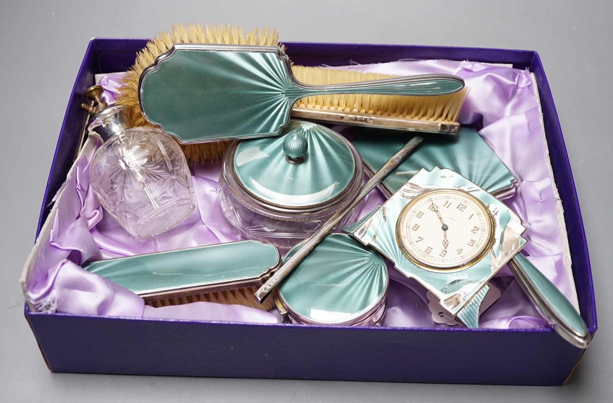 A George V silver and green guilloche enamel set nine piece dressing table set, by Albert Carter, Birmingham, 1933/4, together with a similar unmarked timepiece, comb teeth missing and enamel a.f.